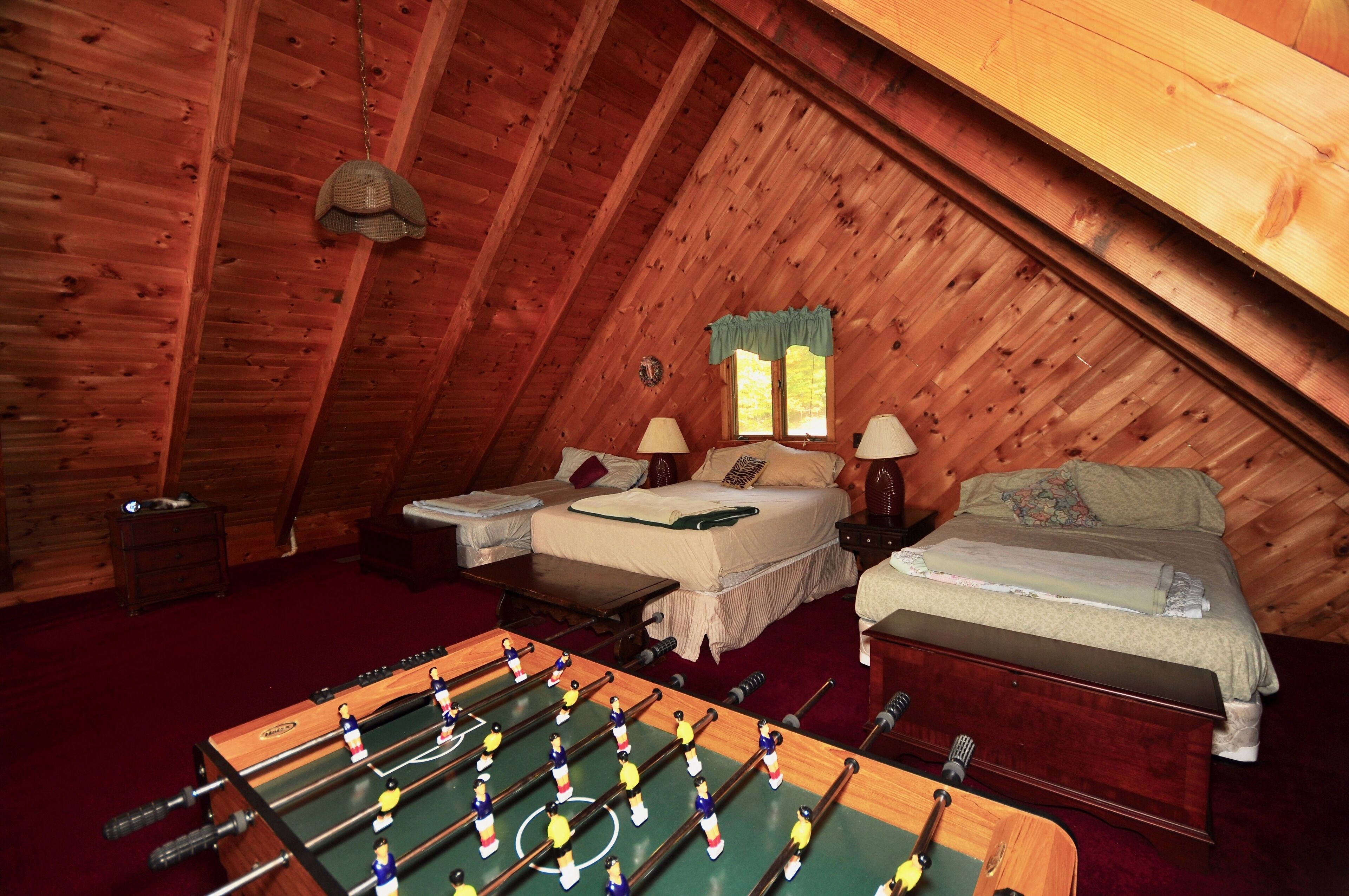 Un dormitorio acogedor en el ático con dos camas, una mesa de futbolín y una ventana con cortinas.