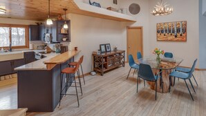 A modern kitchen with a central island, bar stools, and a dining area with a glass table and chairs. - Private Peninsula With 3,000 Feet Of Lakeshore In The Heart Of Lake Country! (Baxter)