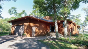 A wooden cabin with a garage, surrounded by trees and a well-maintained lawn. - Private Peninsula With 3,000 Feet Of Lakeshore In The Heart Of Lake Country! (Baxter)