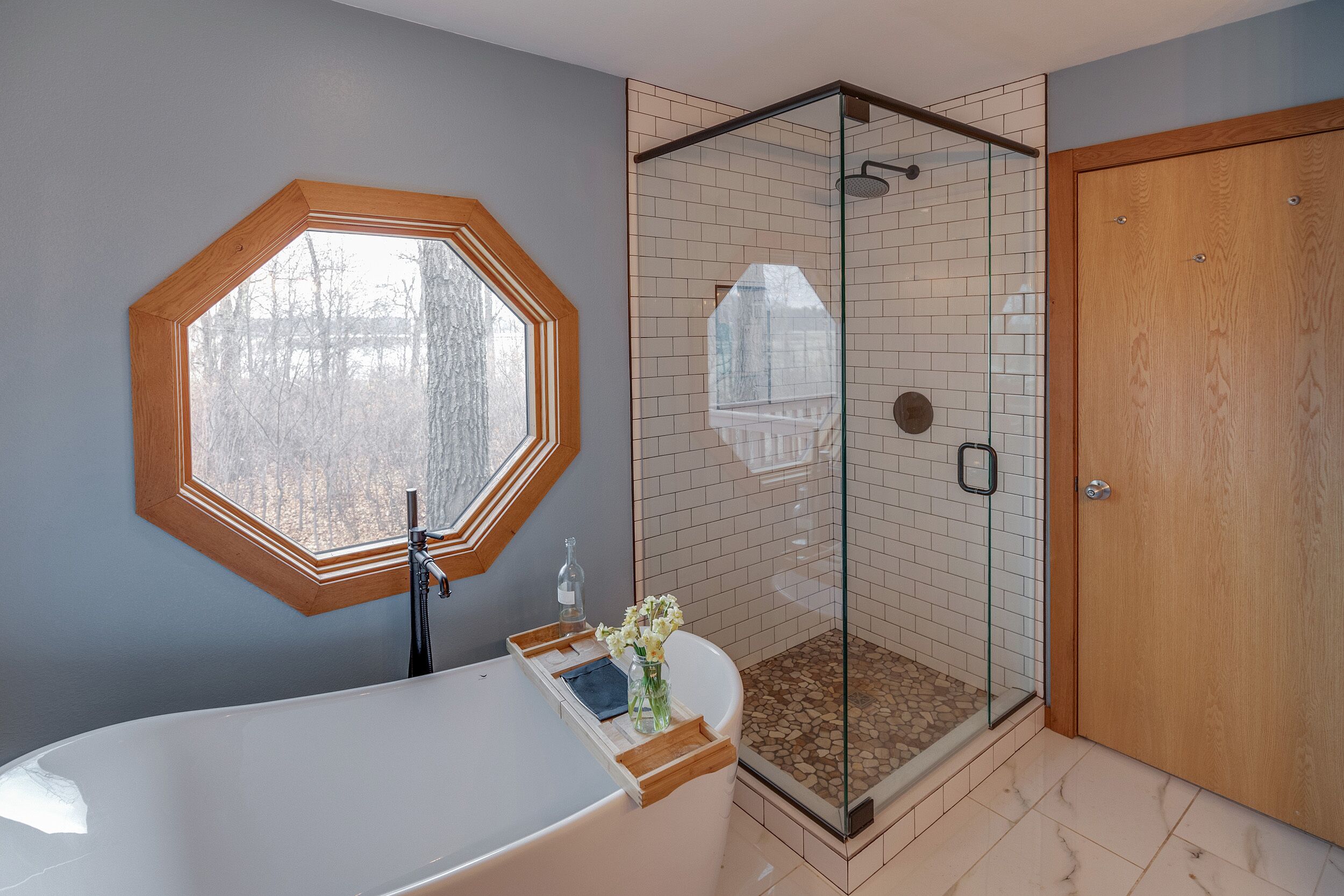 Une salle de bain dotée d’une grande fenêtre octogonale, d’une douche à parois de verre, d’une porte en bois et d’une baignoire.