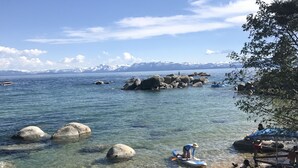 A beach with clear water, rocks, and mountains in the background.