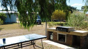 Un patio trasero con una parrilla, una mesa de picnic y un coche aparcado.