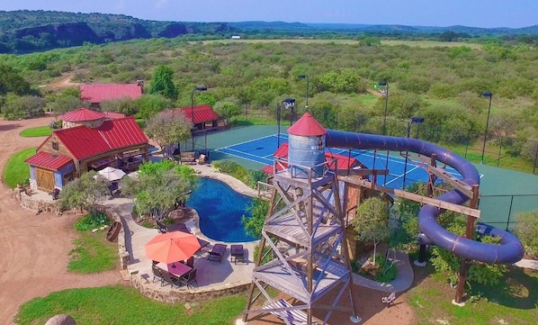 A water park with a swimming pool, a water slide, and a red-roofed building. - Red Sands Ranch River Resort - Private Pool, Tennis, Gym, 4-Story Water Slide! (Mason)