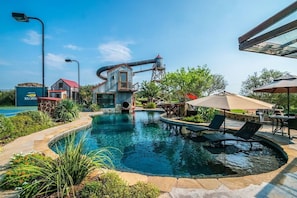 A swimming pool with a water slide, lounge chairs, and outdoor seating. - Red Sands Ranch River Resort - Private Pool, Tennis, Gym, 4-Story Water Slide! (Mason)