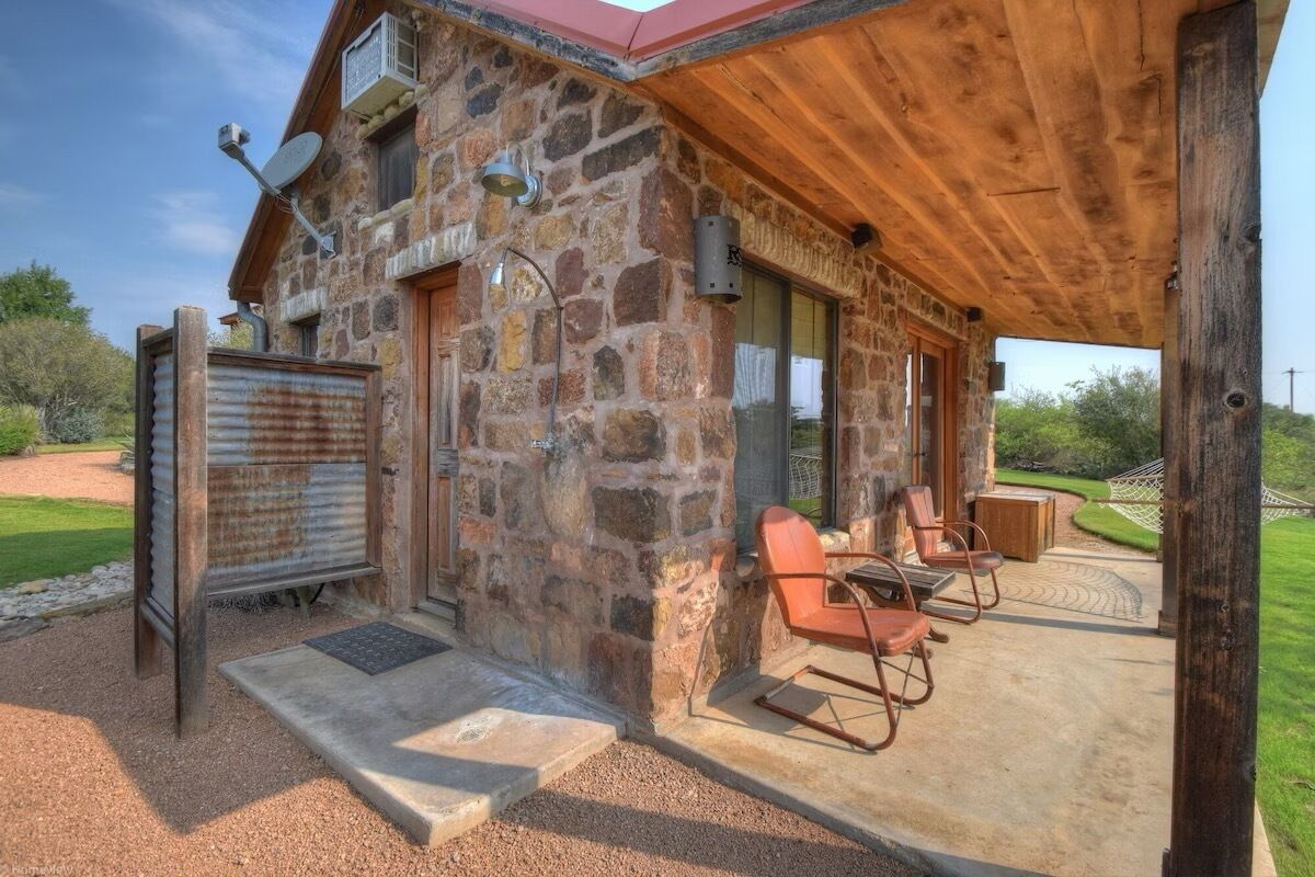 A stone building with a wooden porch, outdoor seating, and a satellite dish.