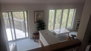 Une pièce avec de grandes fenêtres, une table blanche, un banc et un tableau accroché au mur.