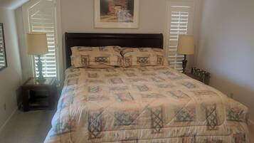 A bedroom with a bed, two bedside tables, two lamps, a framed picture on the wall, and a window with blinds.