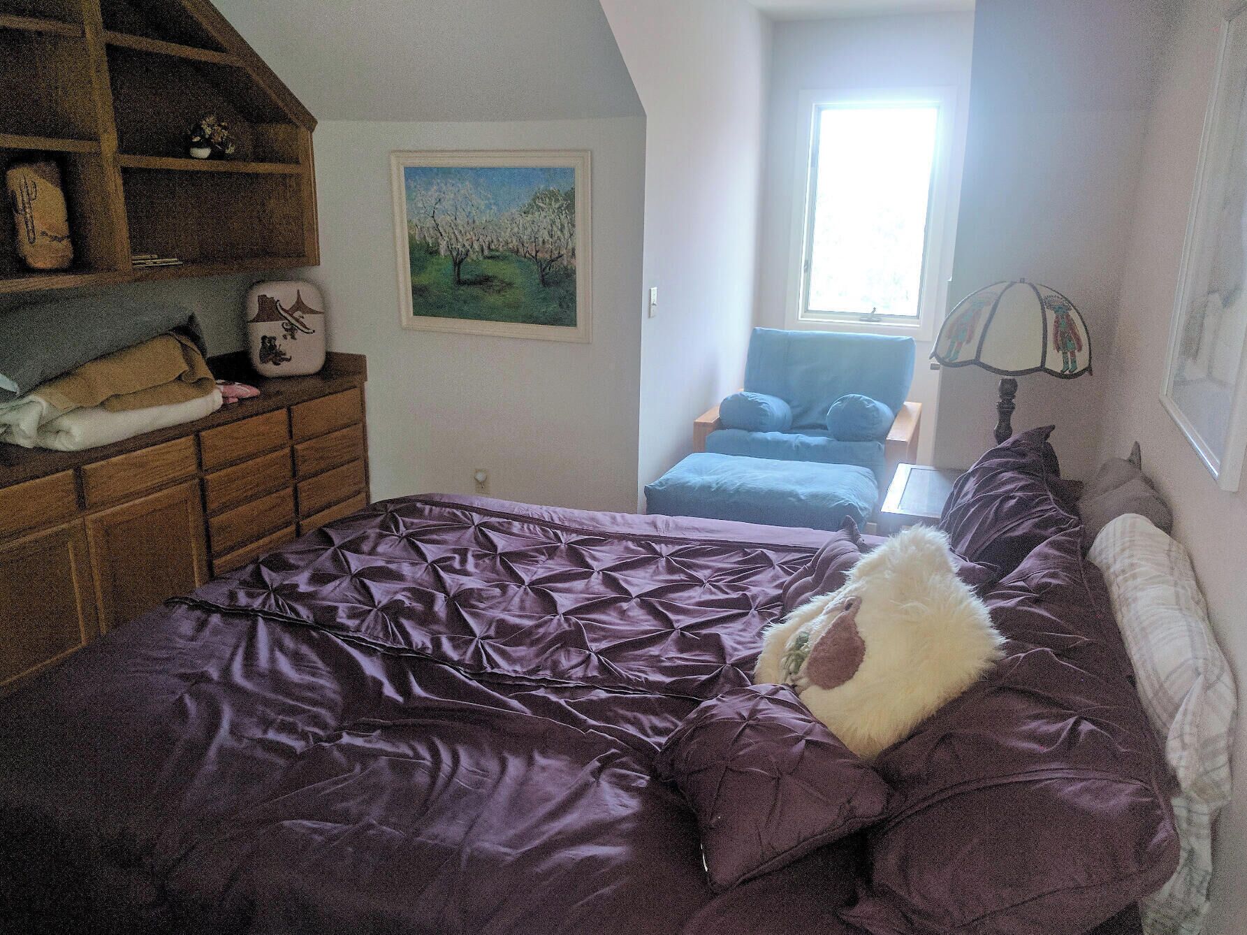 Un dormitorio con una cama grande, un aparador de madera, una silla y un cuadro en la pared.