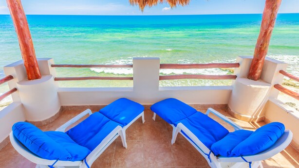 A balcony with two white lounge chairs, each with a blue cushion, overlooking a turquoise sea. - Villa Tranquila-Versatile 4 Bedroom Villa W/Rooftop Pool, Oceanfront . (Isla Mujeres)