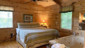A cozy log cabin bedroom with a bed, a vanity with a mirror, a bathtub, and a ceiling fan.
