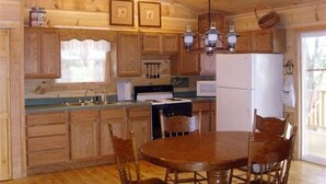 A wooden cabin-style kitchen with a dining table and chairs, a refrigerator, and a stove.