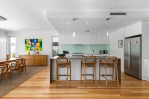 Une cuisine moderne avec des meubles blancs, un réfrigérateur en acier inoxydable et un îlot central doté de tabourets de bar.