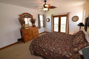 Quarto com cama, penteadeira, espelho, ventilador de teto e janela com cortinas.