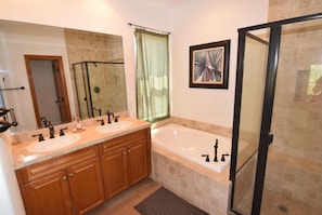 Une salle de bain avec deux lavabos, une baignoire, une douche avec une porte en verre et un tableau encadré au mur.
