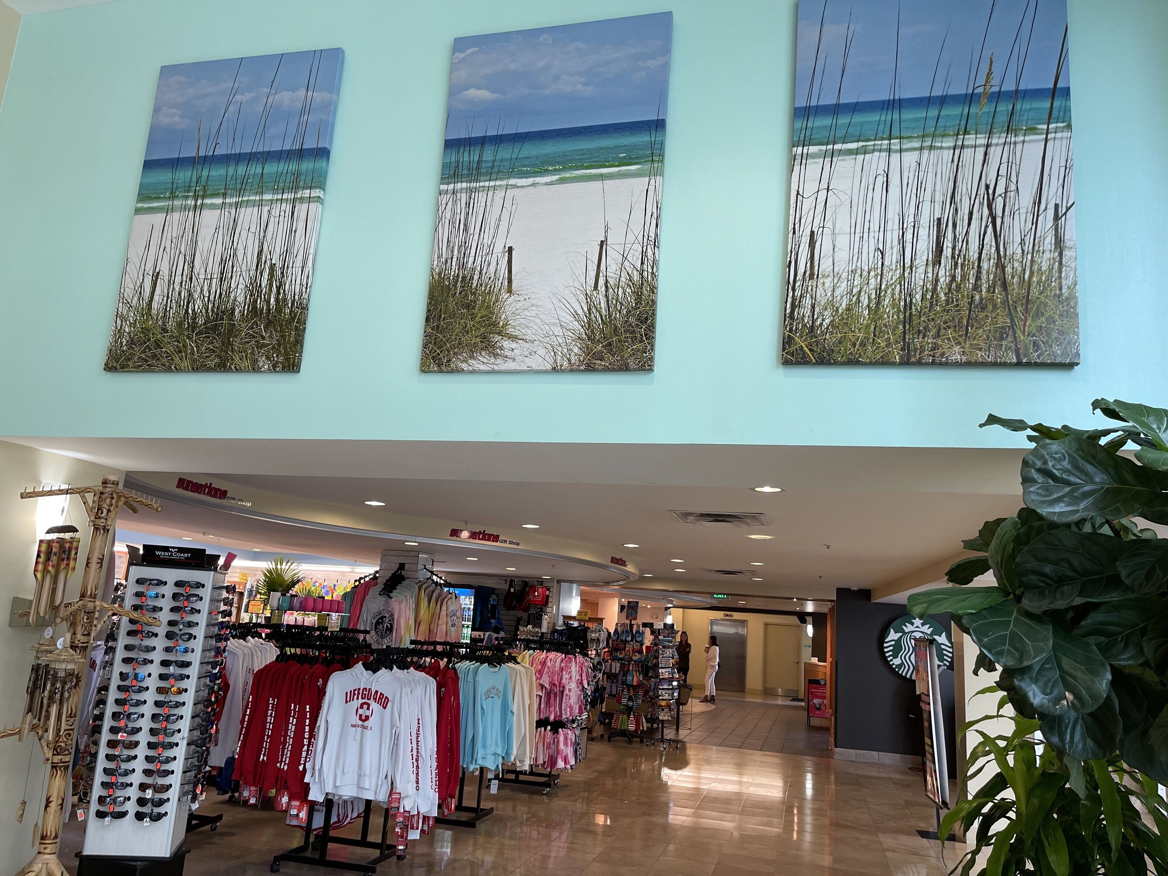 Innenansicht eines Einkaufszentrums mit einem Kleiderständer im Rettungsschwimmer-Design, einer Kiosk-Imbissbude und einem Schild mit dem Schriftzug Starbucks.