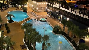Un hotel con varias piscinas, zonas de descanso y una fachada de edificio bien iluminada.