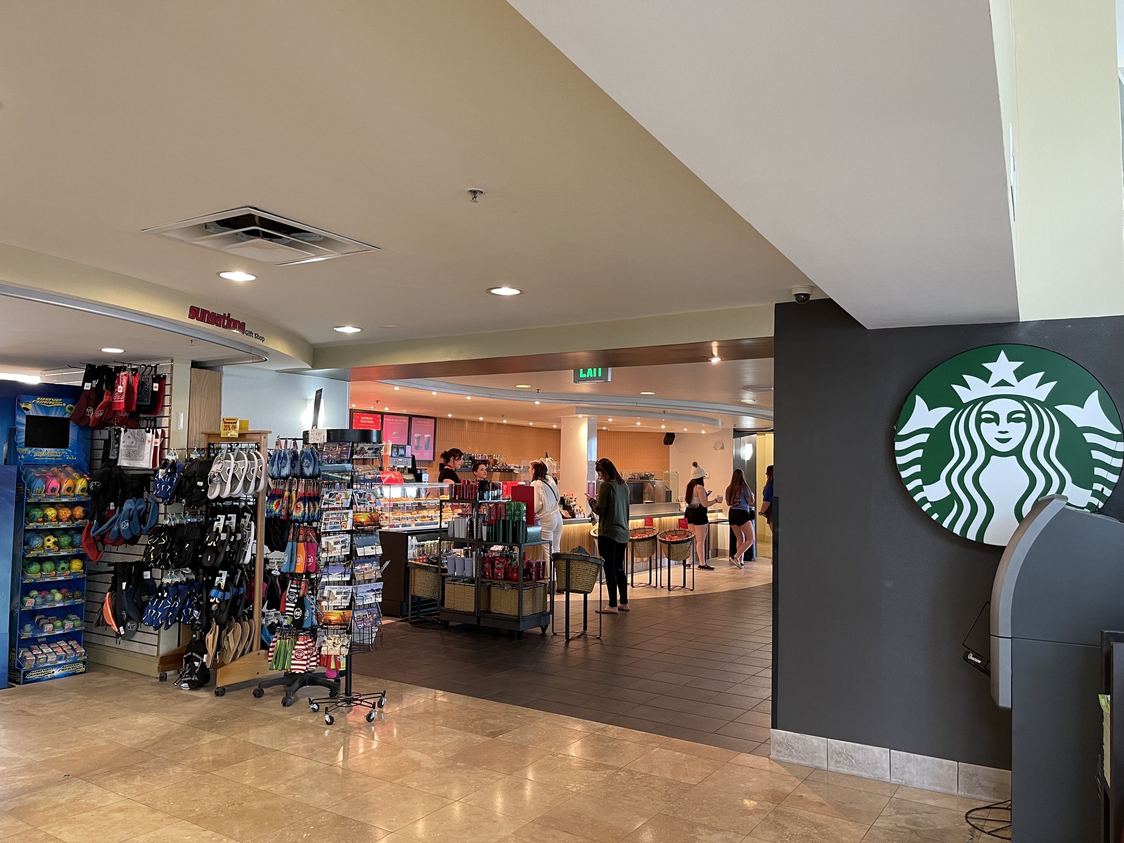 A spacious indoor area with a Starbucks logo, a gift shop, and a seating area with tables and chairs.