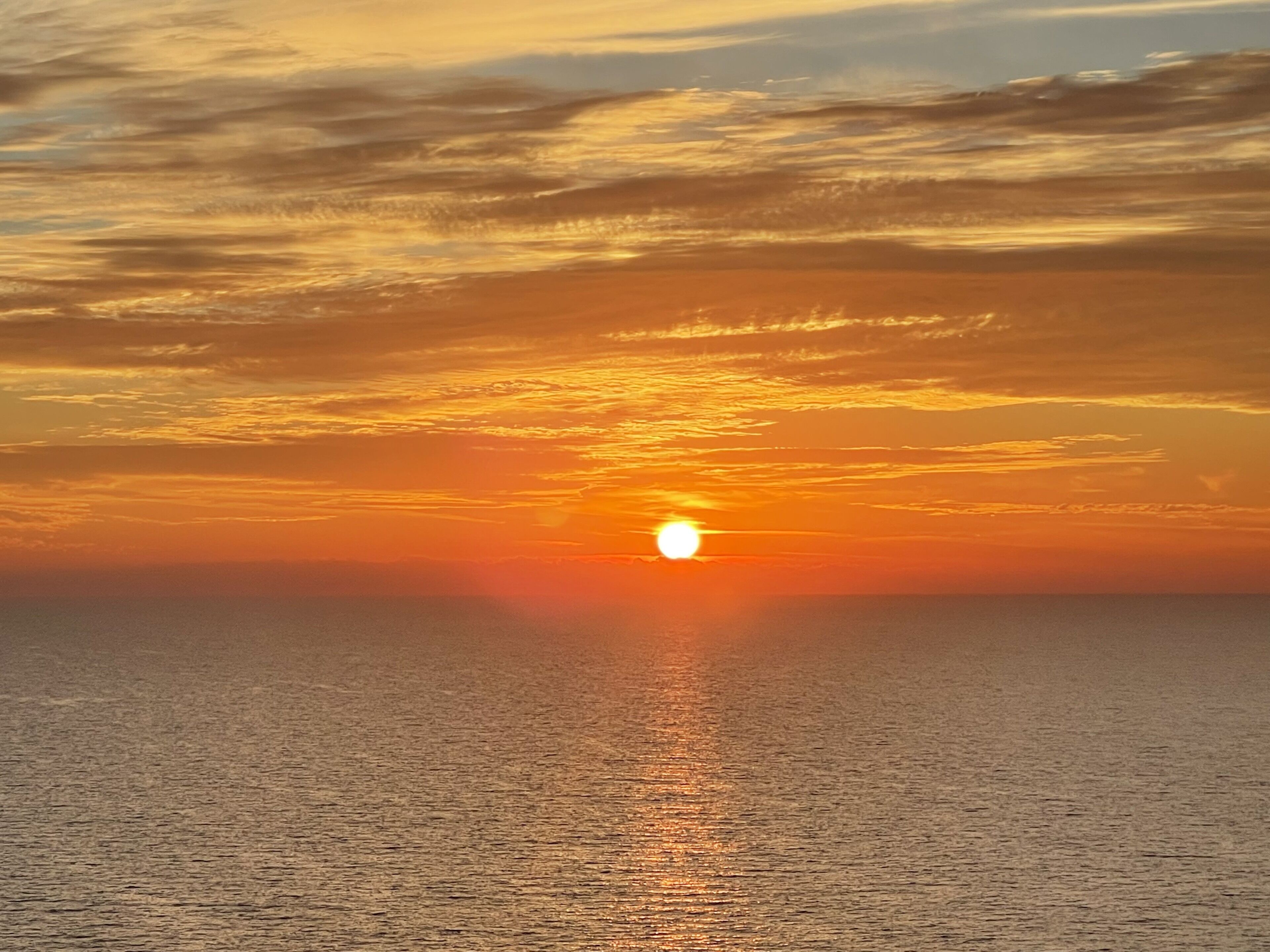 A sunset over a calm sea with a clear sky.