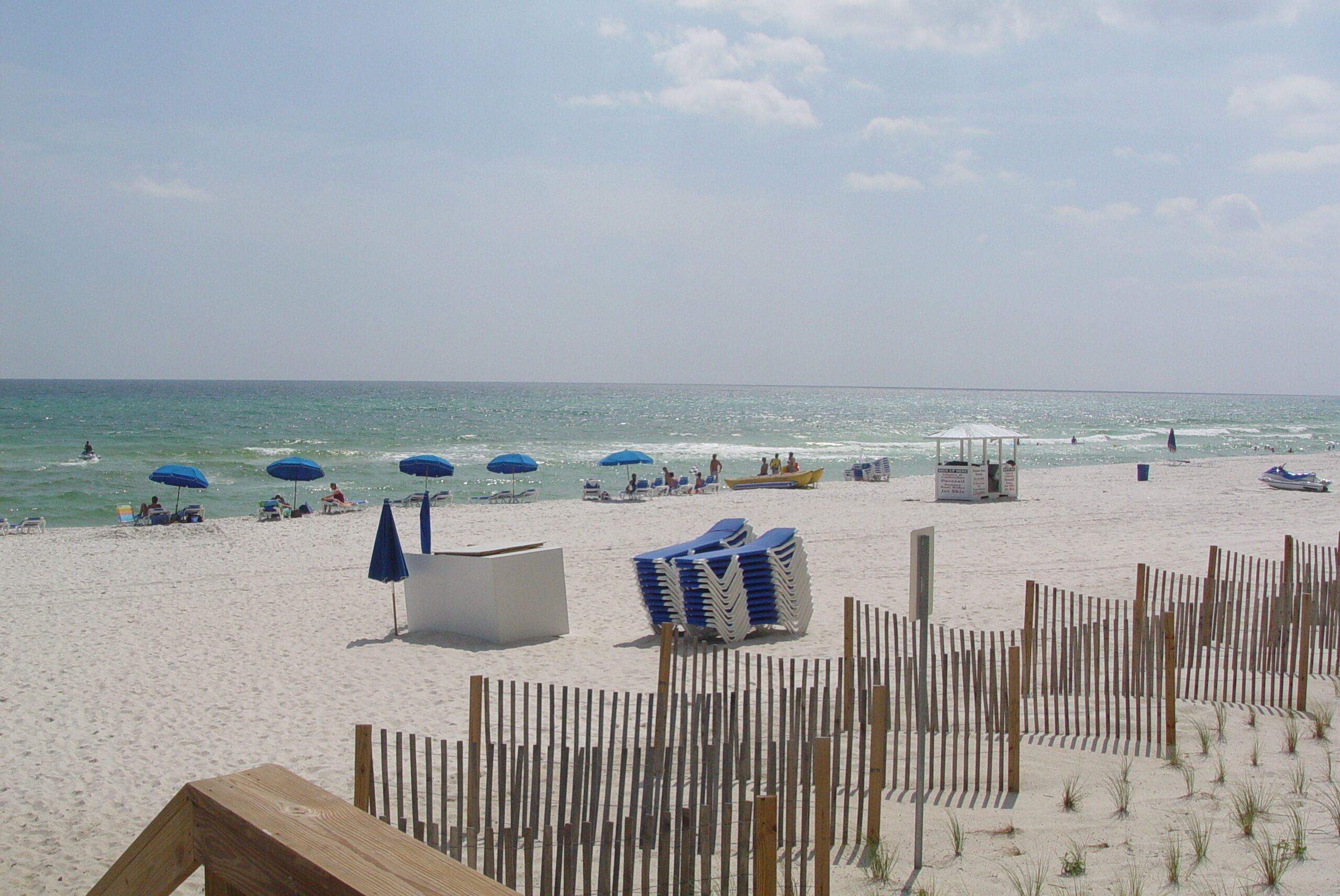 Ein Strand mit Sonnenschirmen, Liegestühlen und einem Holzzaun.