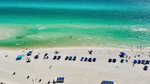 Una playa con aguas turquesas cristalinas, una orilla arenosa y varias sombrillas y sillas de playa azules.