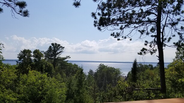 A view from a wooden deck overlooking a lake with dense trees in the foreground and a clear sky. - Beautiful Black Mountain Recreational Area Vacation Rental Cheboygan, MI (Cheboygan)