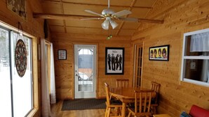 A wooden cabin interior with a dining table, chairs, a red sofa, a ceiling fan, and framed pictures on the walls. - Beautiful Black Mountain Recreational Area Vacation Rental Cheboygan, MI (Cheboygan)