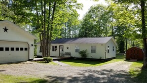 A single-story mobile home with a garage, a small porch, and a fenced yard. - Beautiful Black Mountain Recreational Area Vacation Rental Cheboygan, MI (Cheboygan)