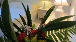Un dormitorio con una cama, mesita de noche, lámpara y una planta con flores.