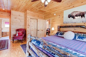 A wooden cabin interior with a bed, a red chair, and a buffalo painting on the wall. - LOG HOME - NEXT TO CREEK / FIREPLACE / HOT TUB / HIKING TRAILS / PET FRIENDLY (Black Mountain)