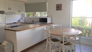 A modern kitchen with white cabinets, a central island, and a dining area with white chairs. - 4/42 Manooka Drive - Rainbow Beach. Stunning Panoramic Views and Swimming Pool (Rainbow Beach)