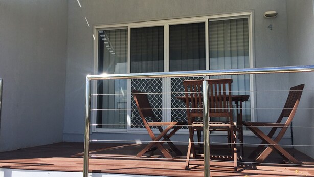 A balcony with a metal railing, a wooden table, and two chairs. - 4/42 Manooka Drive - Rainbow Beach. Stunning Panoramic Views and Swimming Pool (Rainbow Beach)