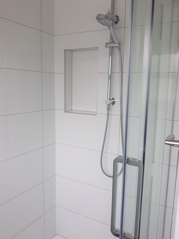 A shower with a handheld showerhead and a fixed showerhead, mounted on a wall with white tiles. - Great House! (Otematata)