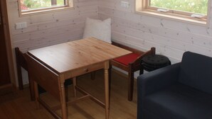 Una habitación con paredes de madera, una mesa de madera, un sofá azul y dos ventanas con vistas a un campo cubierto de césped.