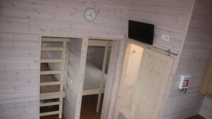 Una habitación pequeña y funcional con una litera, un inodoro y un televisor fijado a la pared.