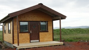 Una pequeña cabaña de madera con un porche, ventanas grandes y una puerta.