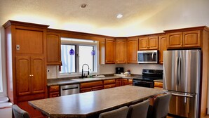 A kitchen with wooden cabinets, a stainless steel refrigerator, a microwave, and a large island with bar stools.