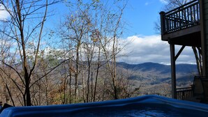 A hot tub with a mountain view, a wooden deck, and a clear sky.