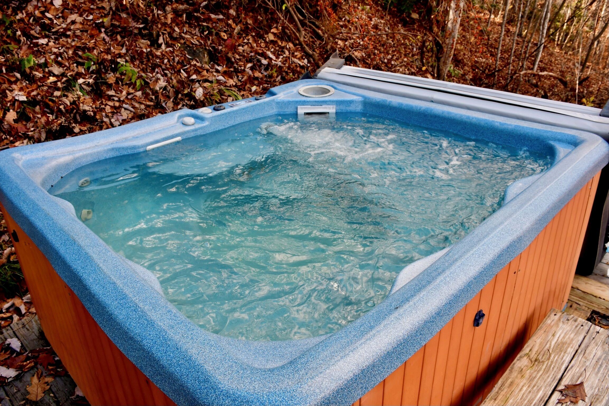 Un bain à remous à l’intérieur bleu, entouré d’une terrasse en bois et d’un sol recouvert de feuilles.