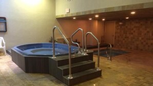 Un jacuzzi con escalones y barandillas metálicas, suelo de baldosas y una pared con textura.