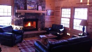 A cozy cabin interior with a stone fireplace, leather sofas, and a plaid rug.