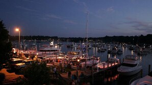 A marina at dusk with boats docked and a crowd of people near the waterfront.