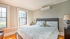 A bedroom with a large bed, a nightstand, a lamp, and a window with a view of greenery. - Perfect Location, Historic Town Ctr: Ground 4 Bed 3 Bath Condo (Provincetown)