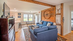 A modern living room with a blue sofa, wooden beams, and a large wooden wheel wall decoration. - Perfect Location, Historic Town Ctr: Ground 4 Bed 3 Bath Condo (Provincetown)
