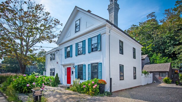 A two-story white house with blue shutters, a red door, and a chimney. - Perfect Location, Historic Town Ctr: Ground 4 Bed 3 Bath Condo (Provincetown)