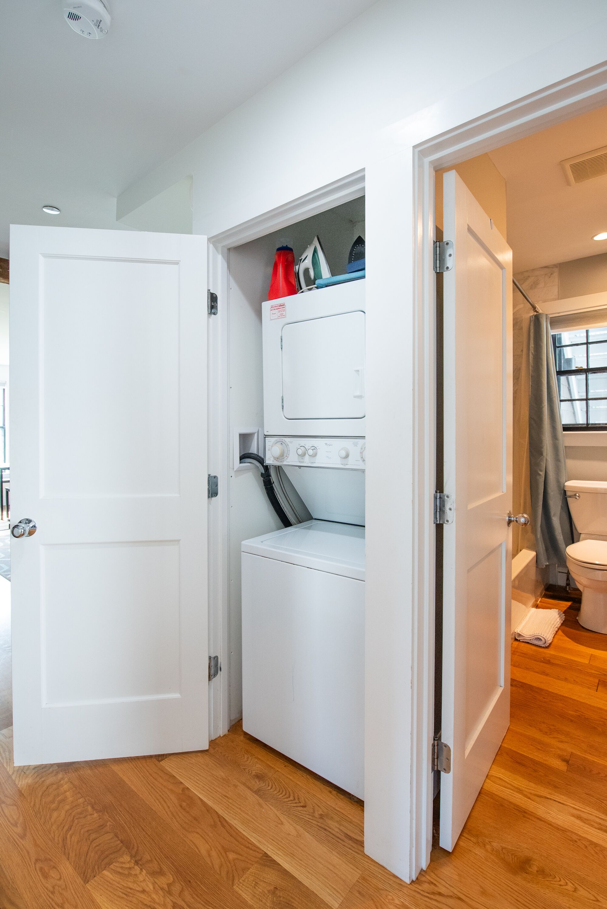 Un lavadero con lavadora y secadora, una puerta que da a otra habitación y una ventana con cortina.