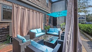 An outdoor patio area with wicker furniture and a glass table, surrounded by a beige curtain. - Perfect Location, Historic Town Ctr: Ground 4 Bed 3 Bath Condo (Provincetown)