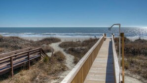 A wooden boardwalk leading to a beach with a clear view of the ocean.