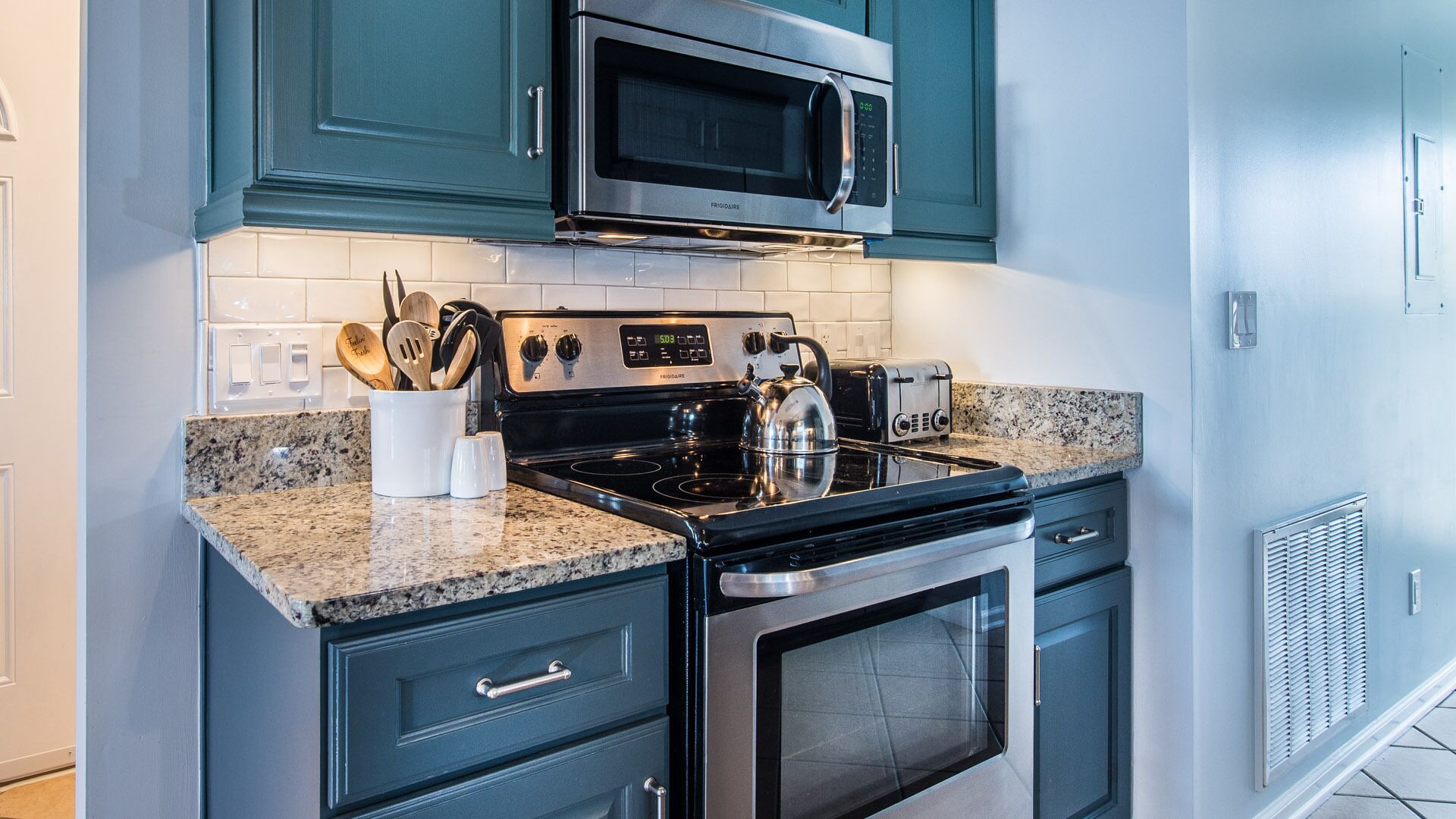 A kitchen with teal cabinets, a stainless steel microwave, a stove, and a toaster.