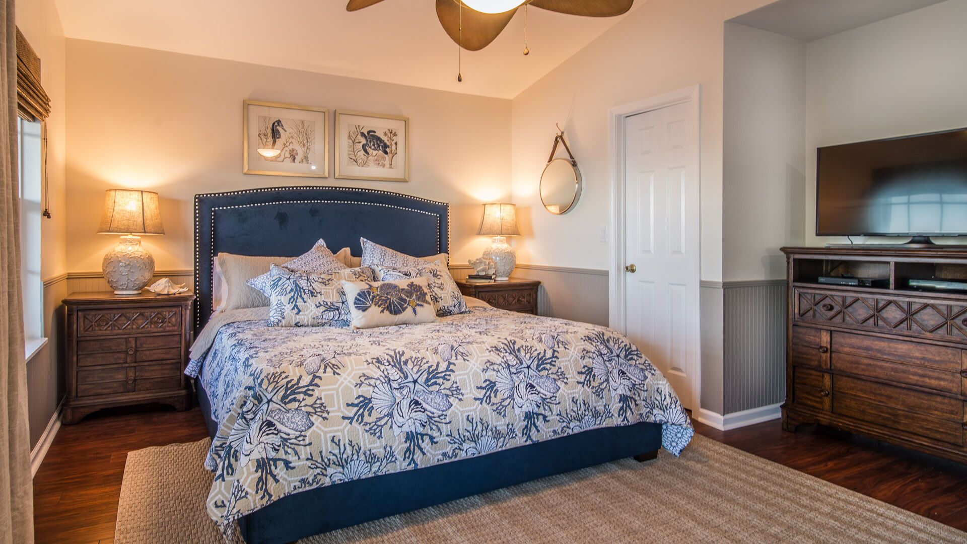 A bedroom with a large bed, two bedside tables, a ceiling fan, and a television on a wooden cabinet.
