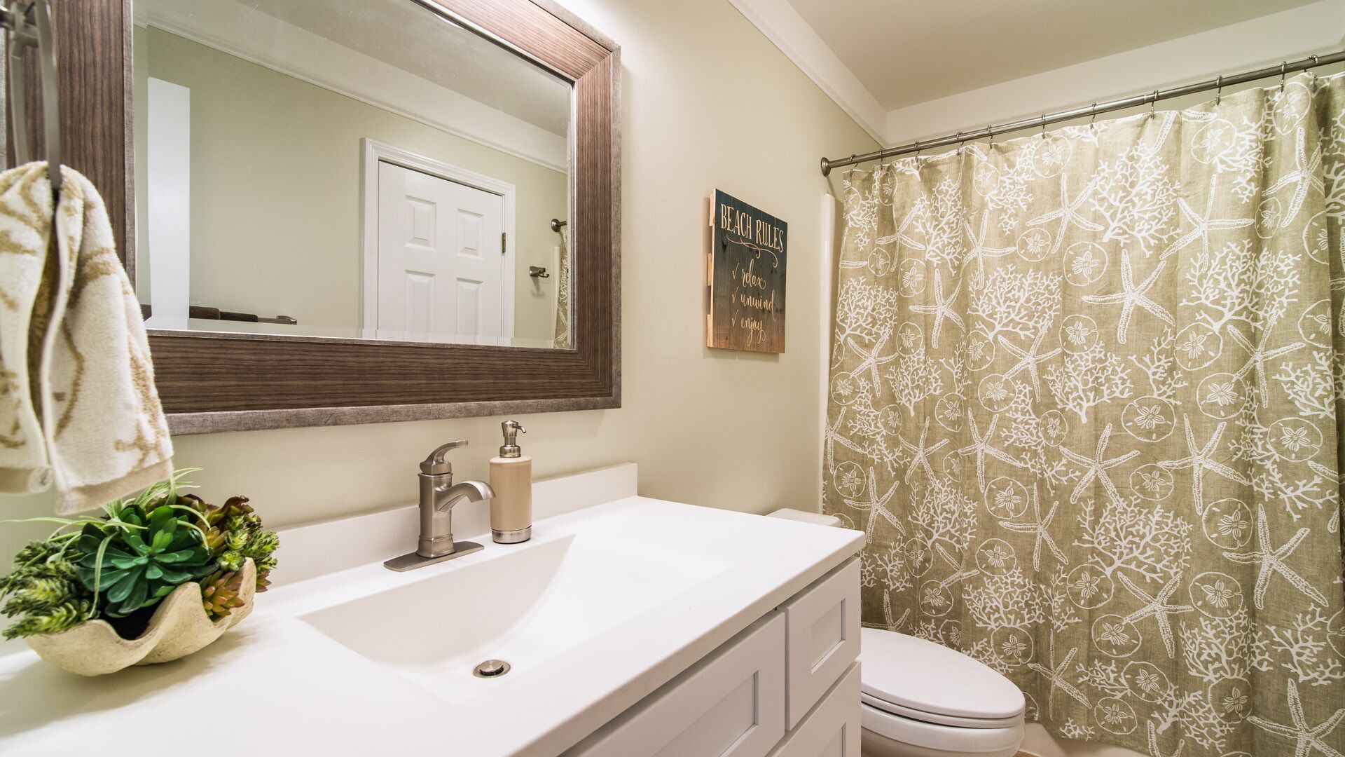 Une salle de bain avec un lavabo blanc, un miroir, des toilettes et un rideau de douche orné d’un motif sur le thème de la mer.